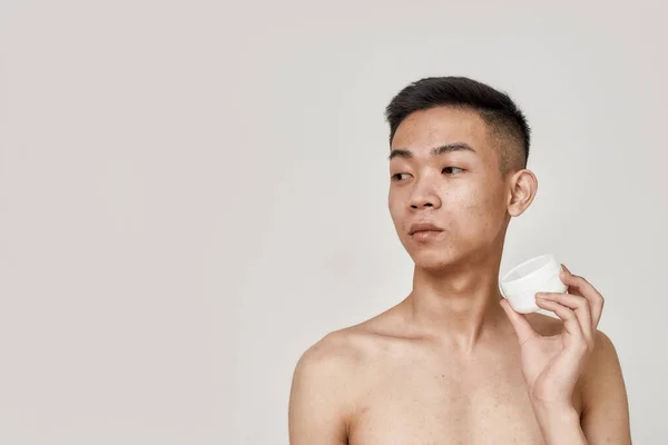 Jól néz ki. Portré félmeztelen fiatal ázsiai férfi tiszta borotvált arc gazdaság krém üveg, reklám bőrápoló termék elszigetelt fehér háttér. Szépség, bőr rutin koncepció — Stock Fotó