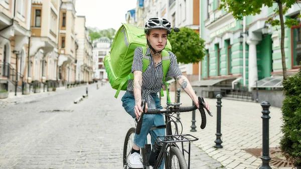 Młoda kobieta w kasku z torbą termiczną lub plecakiem jeżdżąca na rowerze po mieście, dostarczająca jedzenie. Kurier, koncepcja usługi dostawy — Zdjęcie stockowe