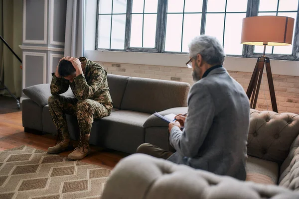 Laat je herinneringen los. Volledige shot van militaire man met hoofd in pijn en depressie tijdens therapie sessie met psycholoog. Soldaat lijdt aan psychologisch trauma. PTSS-concept — Stockfoto