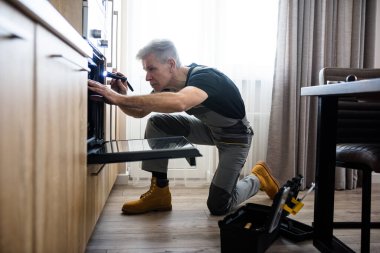 Kişisel teknisyeniniz. Üniformalı bir tamircinin el feneriyle mutfaktaki kırık fırını incelediği uzun bir çekim. Onarım servisi kavramı