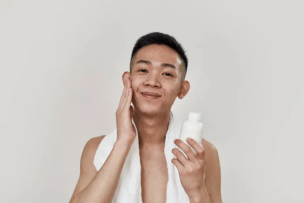 Tökéletes bőr. Portré félmeztelen fiatal ázsiai férfi törülközővel a nyakában nézi kamera, alkalmazása testápoló borotválkozás után elszigetelt fehér háttér — Stock Fotó