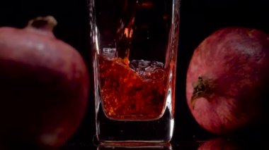 Doğal ve otantik. Şeffaf bir bardağa nar suyu dökerken süper yavaş çekim ve siyah arka plana karşı iki nar. Kapatın. Sağlıklı içecek, vitaminler, meyve konsepti