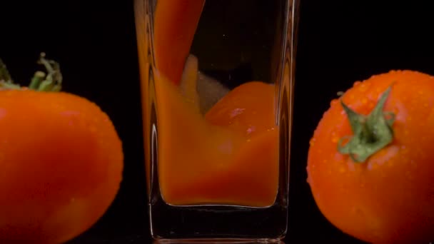 Tomates frescos. Super toma en cámara lenta de verter jugo de tomate en un vaso transparente y dos tomates sobre fondo negro. De cerca. Bebida saludable, concepto de vitaminas — Vídeos de Stock