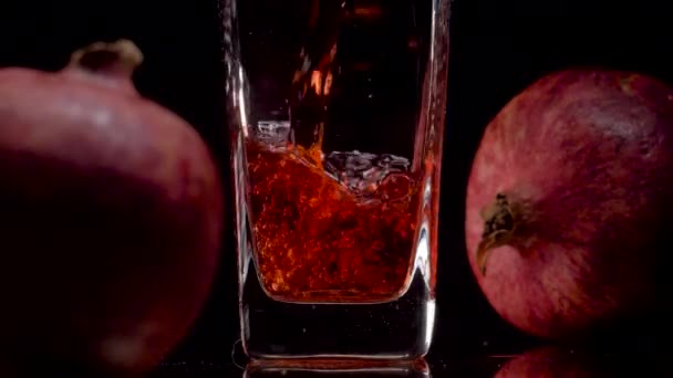 Natürlich und authentisch. Super-Zeitlupenaufnahme des Einfüllens von Granatapfelsaft in ein transparentes Glas und zwei Granatäpfel vor schwarzem Hintergrund. Aus nächster Nähe. Gesundes Getränk, Vitamine, Fruchtkonzept — Stockvideo