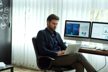 İstatistiksel veriler analiz ediliyor. Genç bir işadamının, finansal analistin ya da satış müdürünün iş yerinde dizüstü bilgisayarla çalışmasının yan görüntüsü.