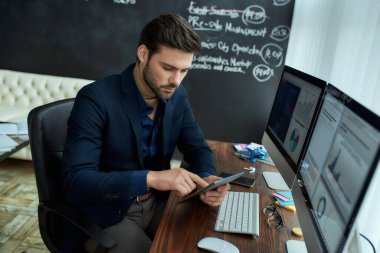 İş analizi. Genç odaklı işadamı, finans analisti veya satış müdürü ofisindeki işyerinde oturup dijital tablet kullanıyor