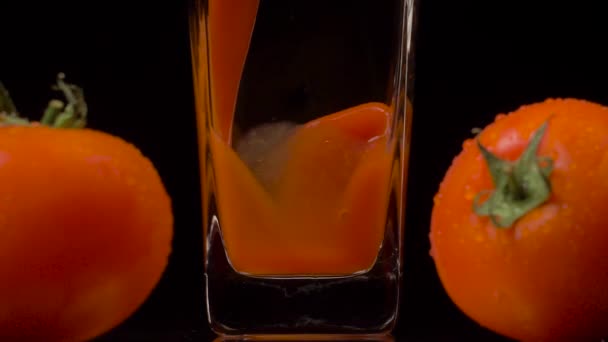 Nur die besten Tomaten. Super-Zeitlupenaufnahme des Einfüllens von Tomatensaft in ein transparentes Glas und zwei Tomaten vor schwarzem Hintergrund. Aus nächster Nähe. Gesundes Getränk, Vitaminkonzept — Stockvideo