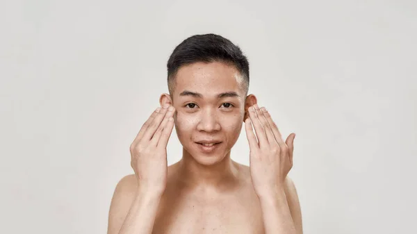 Refresca. Retrato de un joven asiático sin camisa enjuagándose la cara después de afeitarse mirando a la cámara aislada sobre fondo blanco. Belleza, concepto rutinario de cuidado de la piel — Foto de Stock