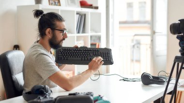 Evde yeni cihazlar hakkında video günlüğü ya da vlog kaydederken elinde klavye olan erkek teknoloji blogcusu