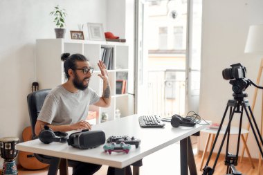 Erkek teknoloji blogcusu el sallıyor, merhaba diyor, video blogu ya da video blogu kaydederken aboneleri selamlıyor ev stüdyosunda yeni cihazlar hakkında