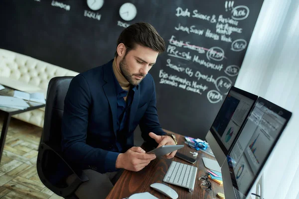 Business analyst at work. Young focused man sitting at his workplace in the office and using digital tablet. Analyzing statistical data, graphs and charts on pc screen — Stock Photo, Image