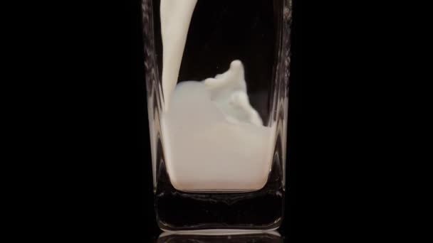 Igyál tejet. Szuper lassított felvétel friss tej öntéséről egy átlátszó pohárba, fekete háttérrel. Közelről. Tejtermék-koncepció — Stock videók