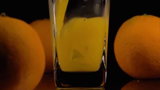自然と新鮮。透明なガラスと黒を背景に2つのオレンジにオレンジジュースを注ぐの超スローモーションショット。閉めろ。健康飲料、ビタミン、果物の概念 — ストック動画