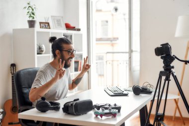Erkek teknoloji blogcusu, video blogu veya video blogu kaydederken aboneler için barış işareti gösteriyor.
