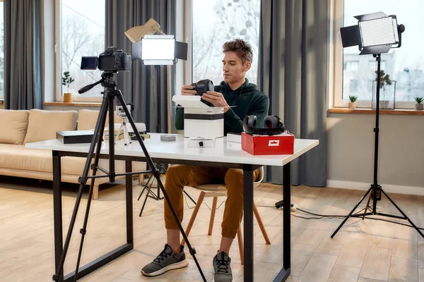 Workplace at home. Full length shot of young male technology blogger recording video blog or vlog about new camera lens and other gadgets at home studio. Blogging, Work from Home concept — Stock Photo, Image