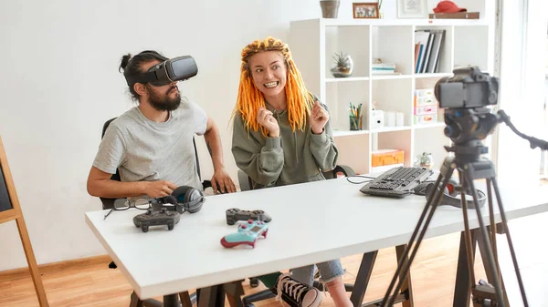 Hombre usando anteojos vr, mientras mujer hablando con la cámara. Joven blogger de tecnología masculina y femenina grabando video blog o vlog sobre nuevos gadgets en casa —  Fotos de Stock