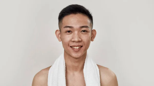 让皮肤呼吸。裸露的年轻亚洲男子的画像，脖子上缠着毛巾，面对着被白色背景隔离的相机微笑。美容、护肤常规概念 — 图库照片