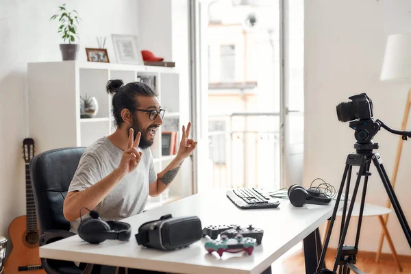 Hombre blogger tecnología mostrando signo de paz para los suscriptores durante la grabación de blog de vídeo o vlog sobre nuevos gadgets en el estudio en casa —  Fotos de Stock