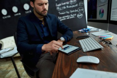 Genç odaklı işadamı ofisindeki işyerinde oturuyor ve dijital tablet kullanıyor, internette finans haberleri okuyor. pc ekranındaki istatistiksel veriler