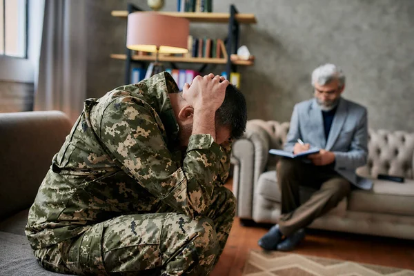 Verwijder je pijn. Militaire man van middelbare leeftijd houdt zijn hoofd in pijn en depressie tijdens therapie sessie met psycholoog. Soldaat lijdt aan psychologisch trauma. PTSS-concept — Stockfoto