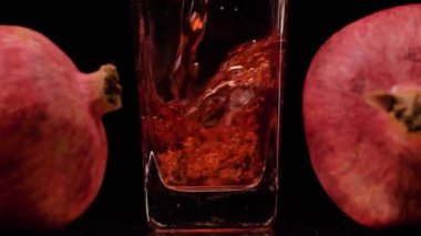 Premium Juice. Şeffaf bir bardağa nar suyu dökerken süper yavaş çekim ve siyah arka plana karşı iki nar. Kapatın. Sağlıklı içecek, vitaminler, meyve konsepti