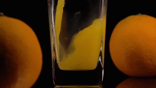 El sabor de la naturaleza. Super toma en cámara lenta de verter jugo de naranja en un vaso transparente y dos naranjas sobre fondo negro. De cerca. Bebida saludable, vitaminas, concepto de frutas — Vídeos de Stock