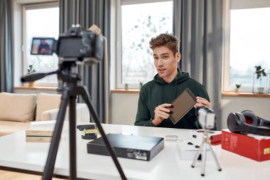 Teknoloji Ruhu. Genç erkek teknoloji blogcusu video blogu veya video blogu kaydediyor. Yeni tablet bilgisayar ve diğer cihazlar hakkında. Bloglama, Evden Çalışma kavramı