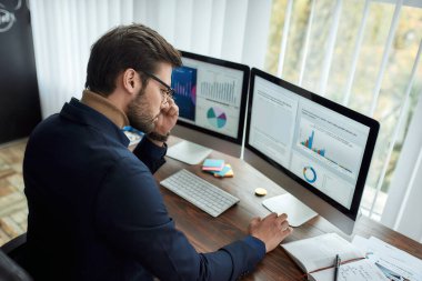Modern ofiste çalışan başarılı iş adamı veya finans analisti, bilgisayar ekranındaki grafik ve grafiklere bakıyor ve istatistiksel verileri analiz ediyor