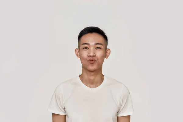 Kyss mig. Porträtt av ung asiatisk man med rent rakat ansikte ser lekfull samtidigt blåser, ger en kyss på kameran isolerad över vit bakgrund. Skönhet, hudvård, ansiktsuttryck — Stockfoto