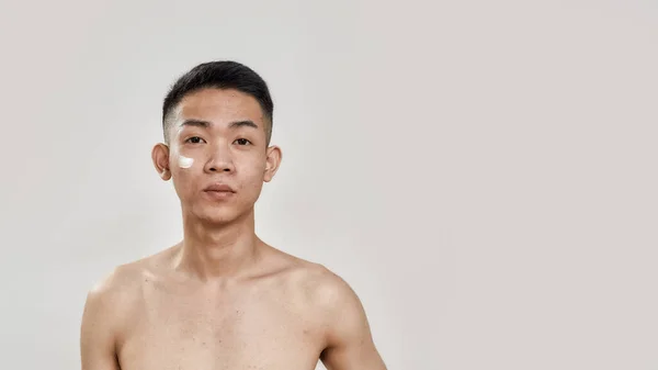 A legjobb a bőrödnek. Póló nélküli fiatal ázsiai férfi arcképe, krémmel az arcán, fehér háttérrel izolált kamerát néz. Szépség, bőr rutin koncepció — Stock Fotó