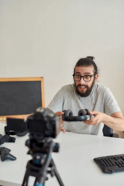 Man teknik bloggare i glasögon ser upphetsad, hålla hörlurar medan du spelar in video blogg eller vlog om nya prylar hemma studio — Stockfoto