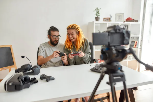 Homem e mulher usando, discutindo joystick controlador de jogo. Jovens blogueiros de tecnologia masculina e feminina gravando vídeo blog ou vlog sobre novos gadgets em casa — Fotografia de Stock