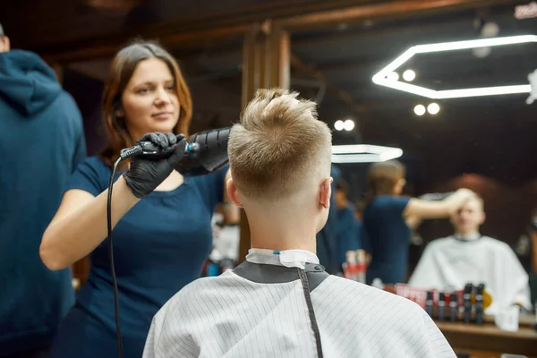 Profesyonel berber kız, genç bir adamın saçını kurutuyor. Aynanın önünde berber koltuğunda oturuyor. — Stok fotoğraf