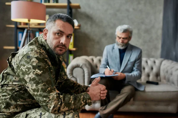 Krijg nog een visioen. Militaire man van middelbare leeftijd kijkt opzij tijdens therapie sessie met psycholoog. Soldaat lijdt aan depressie, psychologisch trauma. PTSS-concept — Stockfoto