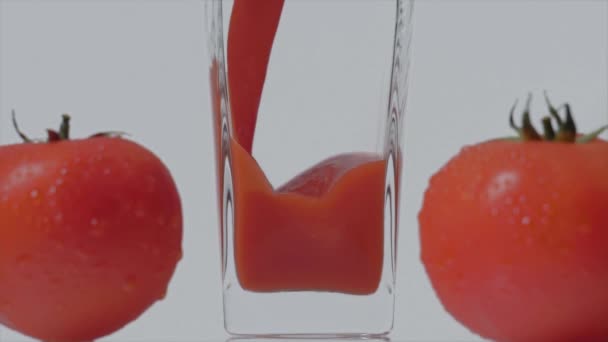 Feinster Geschmack. Super-Zeitlupenaufnahme des Einfüllens von Tomatensaft in ein transparentes Glas und zwei Tomaten vor weißem Hintergrund. Aus nächster Nähe. Gesundes Getränk, Vitaminkonzept — Stockvideo