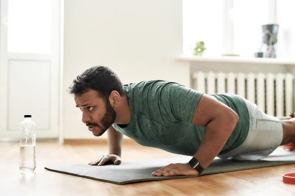 Lucha por un cuerpo en forma. Joven hombre activo buscando centrado, haciendo ejercicio, haciendo flexiones durante el entrenamiento de la mañana en casa. Deporte, estilo de vida saludable — Foto de Stock