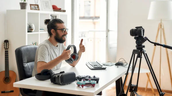 Hombre blogger tecnología celebración de auriculares, mostrando pulgares hacia arriba mientras que la grabación de vídeo blog o vlog sobre nuevos aparatos en el estudio en casa —  Fotos de Stock