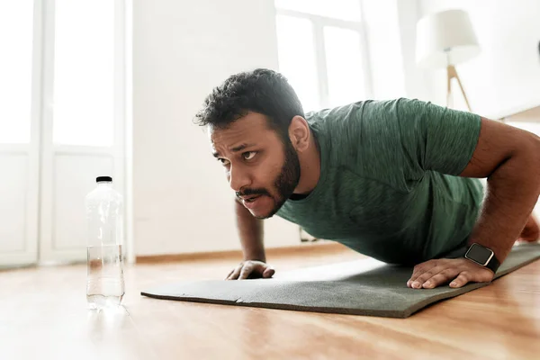 Joven hombre activo buscando centrado, haciendo ejercicio, haciendo flexiones durante el entrenamiento de la mañana en casa. Deporte, estilo de vida saludable — Foto de Stock