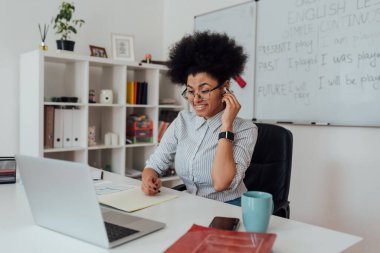 Kablosuz kulaklık takan ve evdeki webcam üzerinden online ders veren mutlu Afro-Amerikan bayan İngilizce öğretmeni.