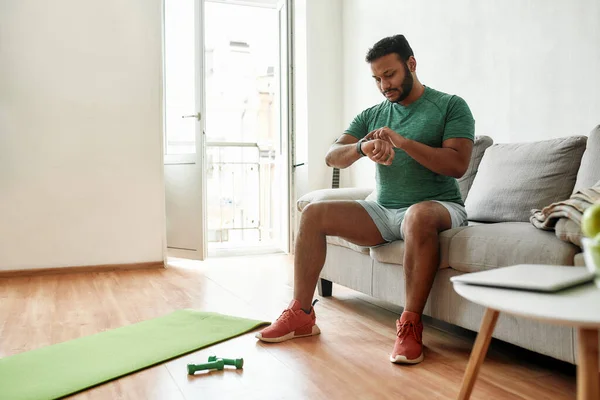 Börja. Full längd skott av ung aktiv man kontrollera tid i smartwatch under pausen, gör morgonträning med hantlar på yogamattan hemma. Motivering och ändamålsenlighet — Stockfoto