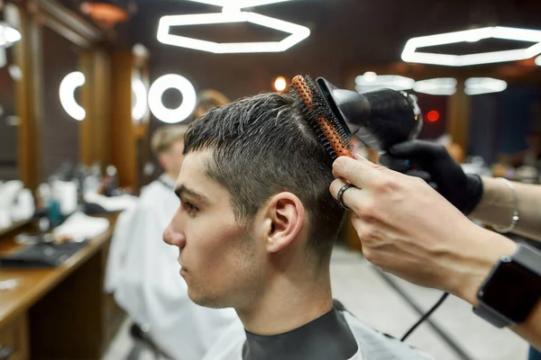 Servire il cliente. Foto ravvicinata del barbiere che asciuga i capelli di un giovane bel ragazzo in visita al moderno barbiere — Foto Stock