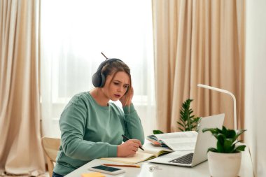Çevrimiçi kursu dinliyorum. Genç odaklı kadın, kulaklık takan kız öğrenci, laptopla masada otururken internette yabancı dil eğitimi alıyor.