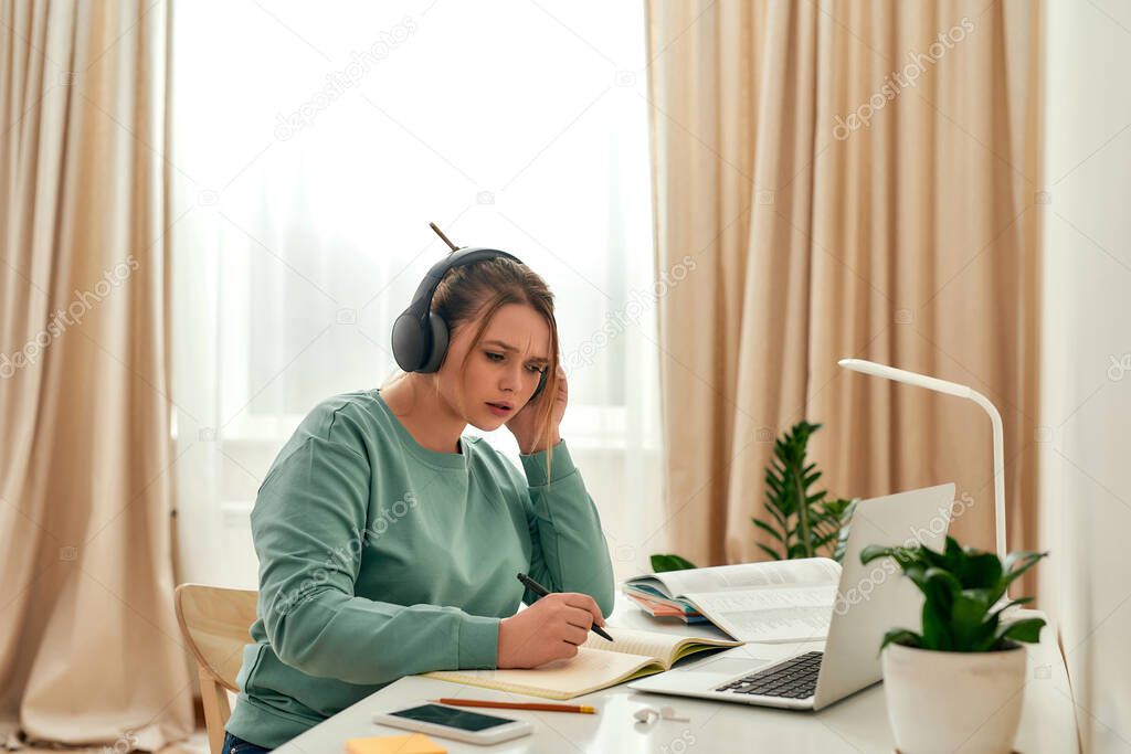 Listening online course. Young focused woman, female student wearing headphones, studying foreign language online while sitting at desk with laptop