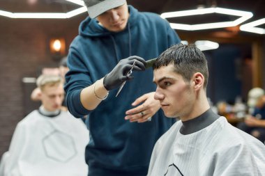 Profesyonel bir erkek berberin berbere ya da kuaföre giden yakışıklı bir genç için yeni moda saç kesimi yaparken yan görüntüsü