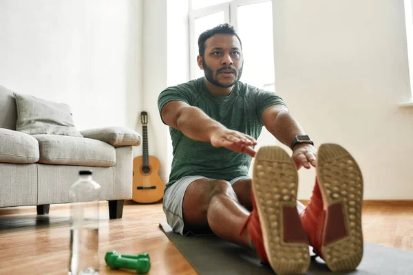 Haz lo mejor que puedas. Joven hombre activo viendo en línea video entrenamiento durante el entrenamiento matutino con mancuernas en la esterilla de yoga en casa — Foto de Stock