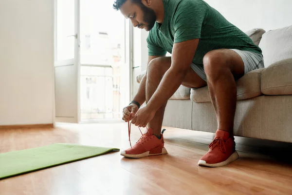 Prepárate. Foto recortada de un joven en zapatillas atando cordones, preparándose para el entrenamiento matutino en una esterilla de yoga en casa. Fitness, concepto de motivación — Foto de Stock