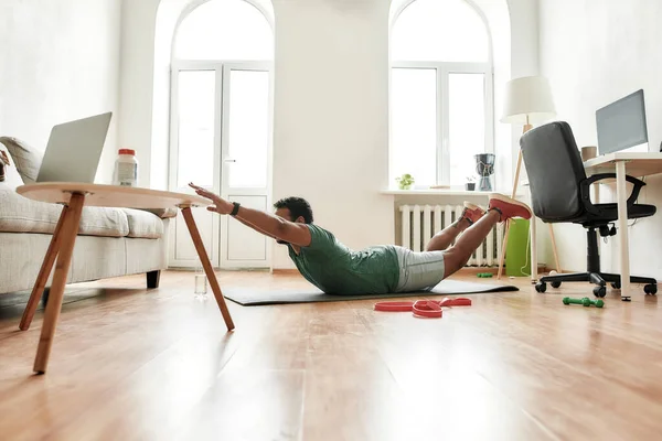 Joven hombre activo buscando enfocado mientras hace ejercicio, estirando el cuerpo durante el entrenamiento de la mañana en casa. Deporte, estilo de vida saludable — Foto de Stock