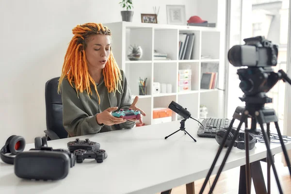 가정에서 마이크를 사용하여 새로운 가젯의 비디오를 녹화하는 동안 게임 컨트롤러 조이스틱을 들고 있는 레게 락이 있는 여성 기술 블로거 — 스톡 사진