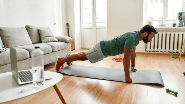 Concéntrate en tus objetivos. Joven hombre activo buscando centrado, haciendo ejercicio, haciendo tablón durante el entrenamiento de la mañana en casa. Deporte, estilo de vida saludable — Foto de Stock