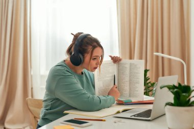 Genç, güzel bir kız, kulaklıklı bir bayan öğrenci öğretmeniyle ya da öğretmeniyle çevrimiçi ders alıyor, evde yabancı diller okuyor.